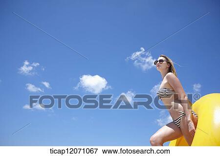Stock Photo - a lady in bikini and beach tube under bright sky. Fotosearch