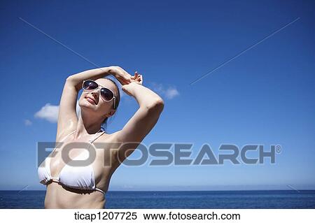 Stock Photography - a lady in bikini and sunglasses posing under bright sky. Fotosearch