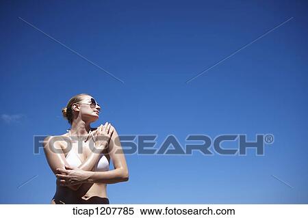 Stock Photography - a lady in bikini and sunglasses posing under bright sky. Fotosearch