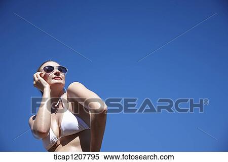 Stock Photography - a lady in bikini and sunglasses posing under bright sky. Fotosearch