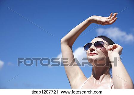 Stock Image - a lady in bikini and sunglasses under bright sky. Fotosearch