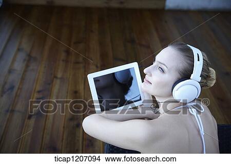 Picture - a lady in bikini lying on a beach bed listening to a music. Fotosearch