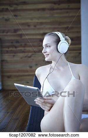 Stock Image - a lady in bikini lying on a beach bed listening to a music. Fotosearch