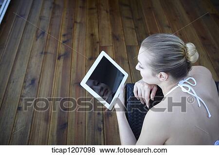 Stock Photo - a lady in bikini lying on a beach bed using tablet PC. Fotosearch