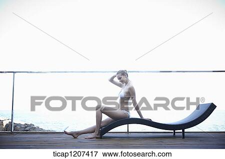 Stock Photo - a lady in bikini posing while sitting on a beach bed. Fotosearch