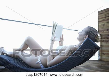 a lady in bikini reading a book while lying on a beach bed View Large Photo Image Picture - a lady in bikini reading a book while lying on a beach bed. Fotosearch