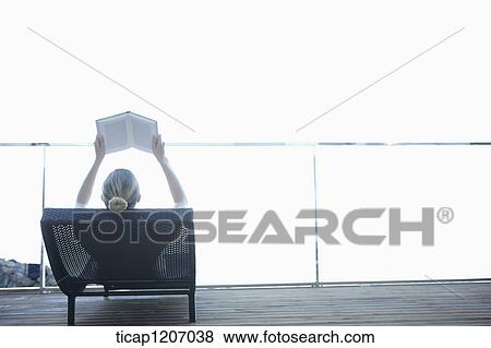 Stock Photo - a lady in bikini reading a book while lying on a beach bed. Fotosearch