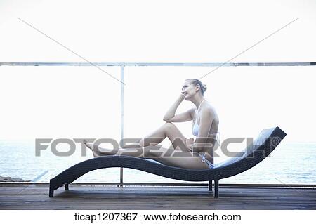 Stock Photo - a lady in bikini sitting on a beach bed. Fotosearch