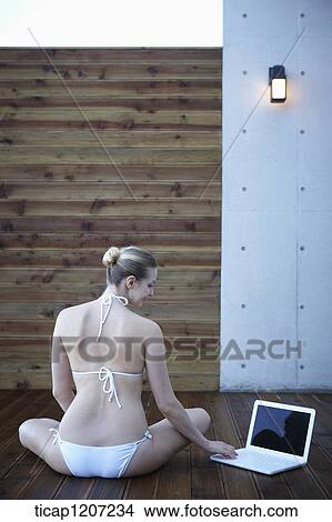 a lady in bikini using laptop while sitting on wooden floor View Large Photo Image Picture - a lady in bikini using laptop while sitting on wooden floor. Fotosearch