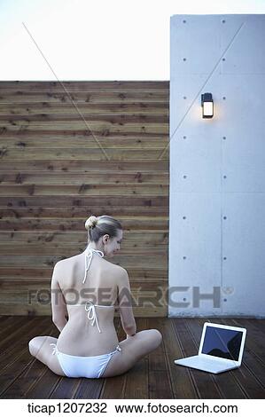 a lady in bikini using laptop while sitting on wooden floor View Large Photo Image Stock Image - a lady in bikini using laptop while sitting on wooden floor. Fotosearch