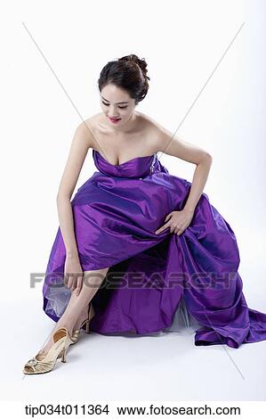Picture - a lady in fancy purple dress putting on the heels. Fotosearch