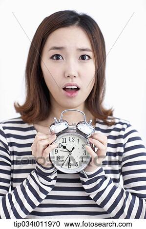 Stock Image - a lady in striped clothes looking worried holding alarm clock. Fotosearch