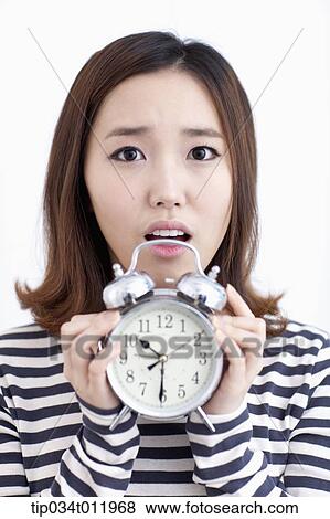 Stock Photo - a lady in striped clothes looking worried holding alarm clock. Fotosearch