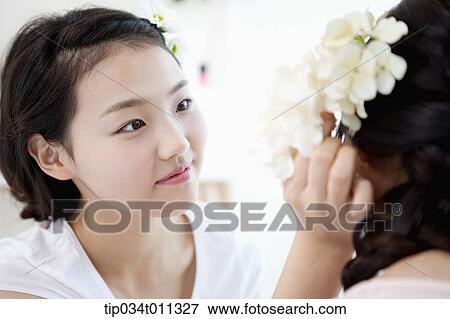 Stock Photo - a lady putting a flower on her friend's hair. Fotosearch