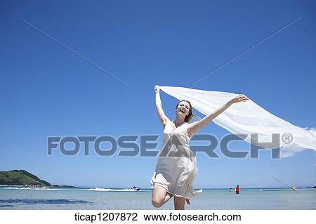 Stock Image - a lady running on the beach with white cloth. Fotosearch