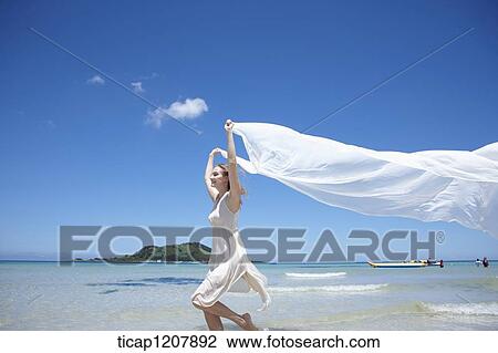 Stock Image - a lady running on the beach with white cloth. Fotosearch