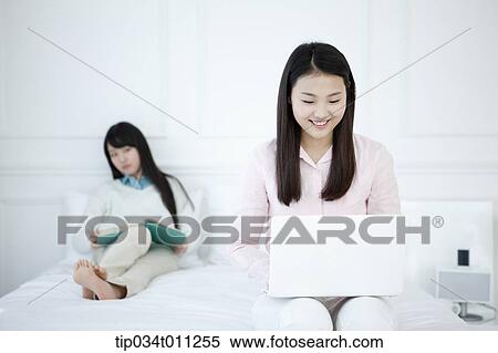 Stock Photography - a lady using a laptop while other lady is reading a book. Fotosearch