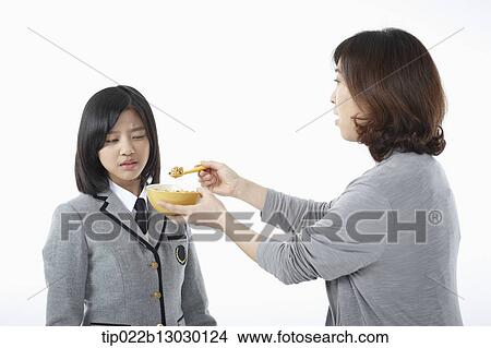 Picture - a mother giving cereal to daughter in a school uniform. Fotosearch