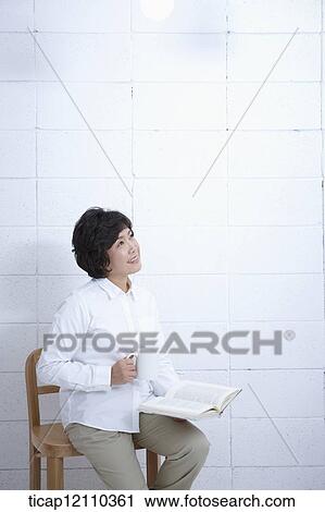 Stock Image - a mother sitting on a chair reading a book. Fotosearch