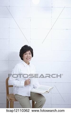 Stock Image - a mother sitting on a chair reading a book. Fotosearch