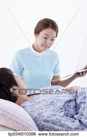 Stock Photo - a nurse standing next to a patient on a bed. Fotosearch