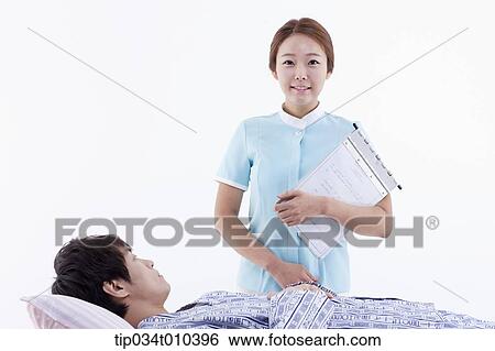 Stock Photograph - a nurse standing next to a patient on a bed. Fotosearch