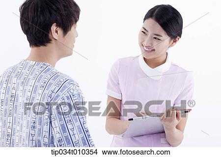 Picture - a nurse writing on a report while talking to a patient. Fotosearch