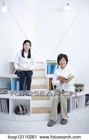 Stock Image - a student and mother sitting on bookshelf reading. Fotosearch