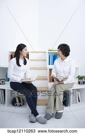 Stock Image - a student and mother sitting on bookshelf reading. Fotosearch