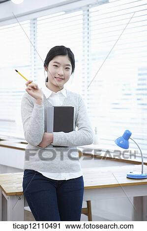 Stock Image - a student holding a book in classroom. Fotosearch