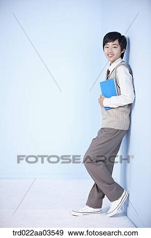 Stock Photo - a student in uniform holding a book while leaning on the wall. Fotosearch