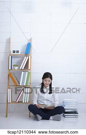 Picture - a student reading a book while sitting on the floor. Fotosearch