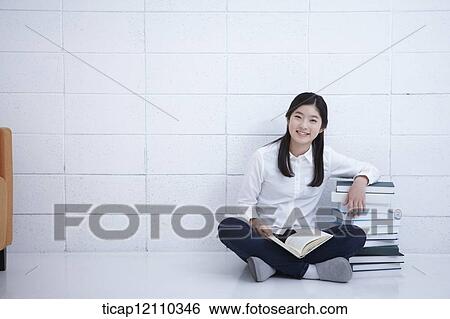Stock Photograph - a student reading a book while sitting on the floor. Fotosearch