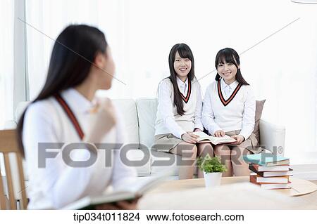 Picture - a student sitting at desk talking to her friends on a couch. Fotosearch