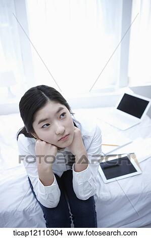 Picture - a student sitting on a bed thinking. Fotosearch