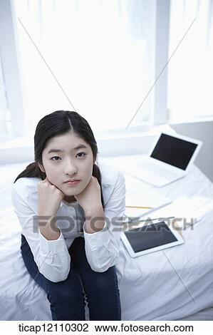 Stock Image - a student sitting on a bed thinking. Fotosearch