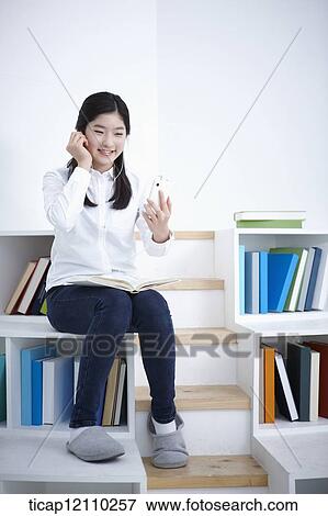 Stock Photo - a student sitting on bookshelf listening to music. Fotosearch