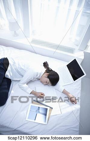 Stock Photograph - a student sleeping on bed while studying. Fotosearch