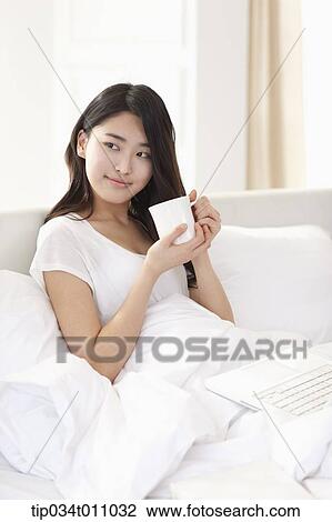 Stock Image - a woman drinking coffee on the bed. Fotosearch