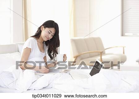 Stock Photo - a woman drinking coffee on the bed. Fotosearch