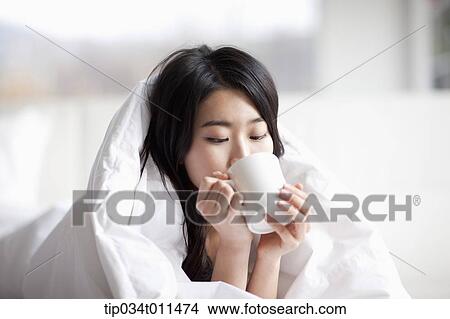 a woman drinking cup of coffee while wrapped in blanket View Large Photo Image Picture - a woman drinking cup of coffee while wrapped in blanket. Fotosearch