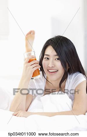 Stock Image - a woman holding a glass of juice on the bed. Fotosearch
