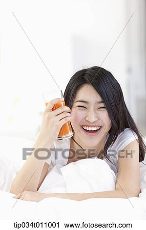 Stock Image - a woman holding a glass of juice on the bed. Fotosearch