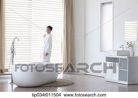 Picture - a woman in bathrobe standing in a bath room. Fotosearch
