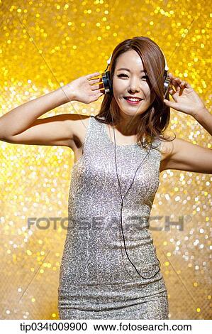 Stock Image - a woman in fancy dress listening to music with headphone. Fotosearch