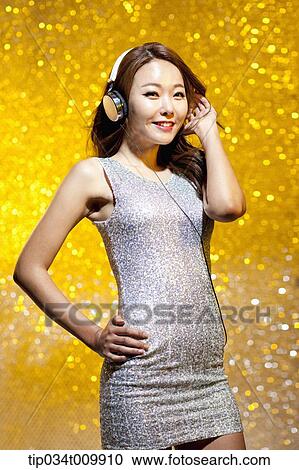 Stock Image - a woman in fancy dress listening to music with headphone. Fotosearch