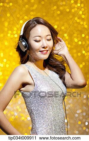 Stock Image - a woman in fancy dress listening to music with headphone. Fotosearch