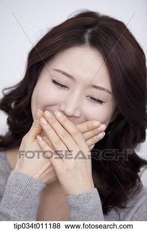 Stock Photo - a woman in grey plain shirt smiling with hands covering. Fotosearch