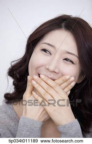 Stock Photo - a woman in grey plain shirt smiling with hands covering. Fotosearch