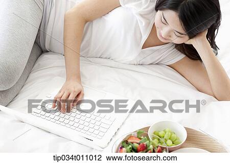 Stock Image - a woman lying on the bed next to breakfast. Fotosearch